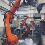 Industrial robot arm handling high-strength custom metal parts on an automated forging production line, ensuring extreme durability and manufacturing consistency for Tier 1 industrial applications.